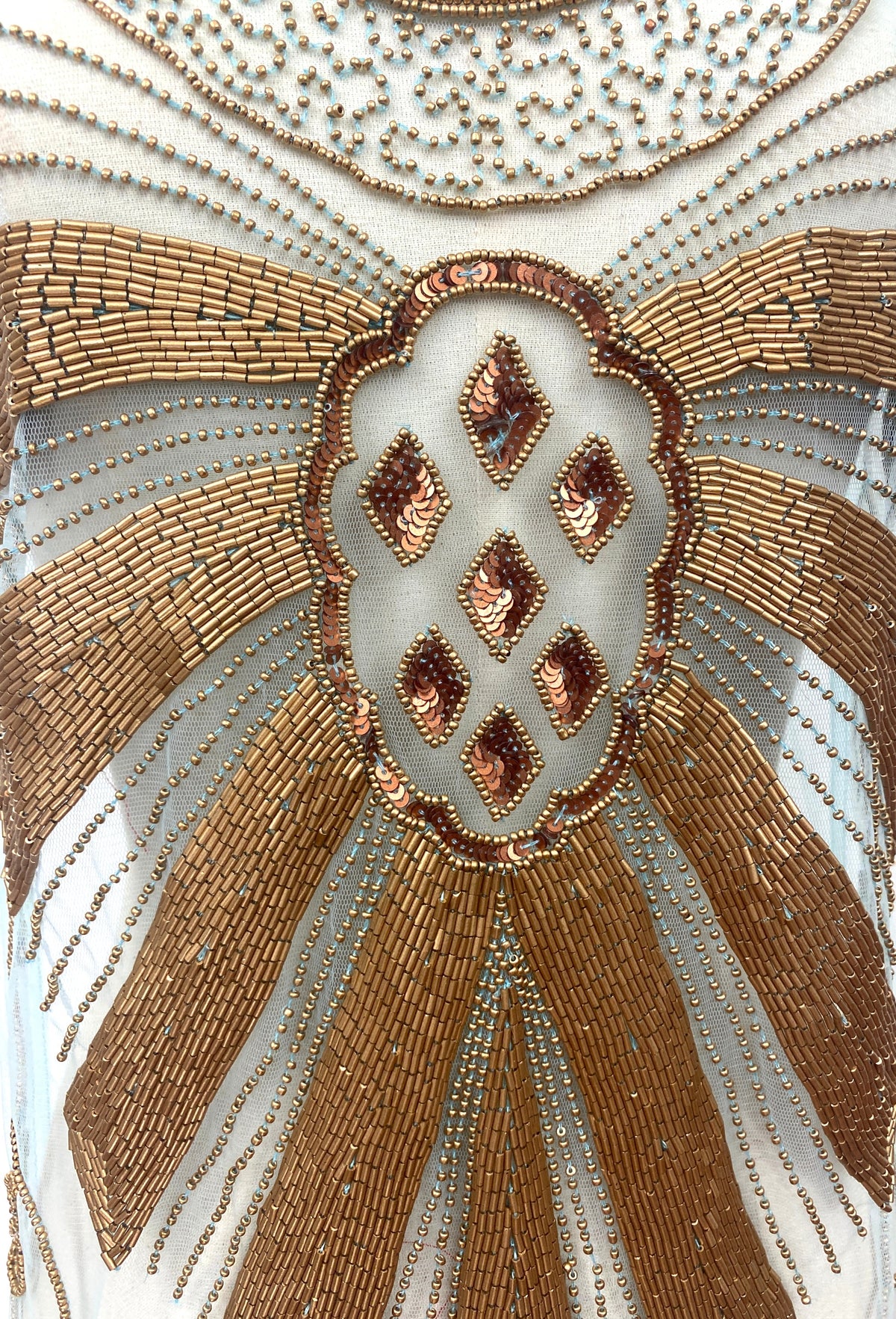 Close-up of gold and turquoise beaded emblem with diamond-shaped accents on overlay
