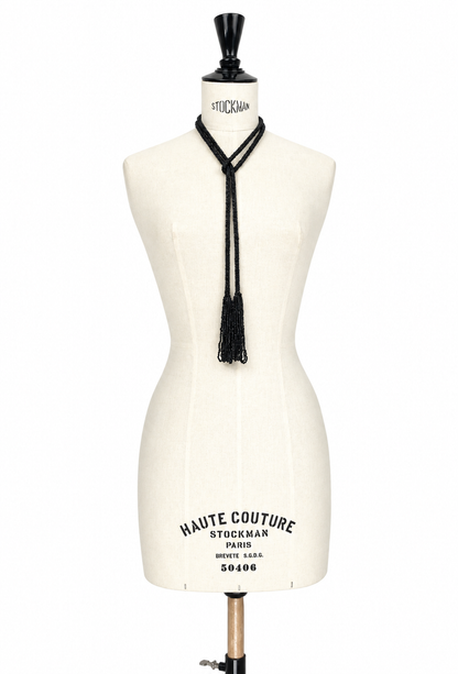 Black lariat necklace with hanging tassel cords on cream mannequin