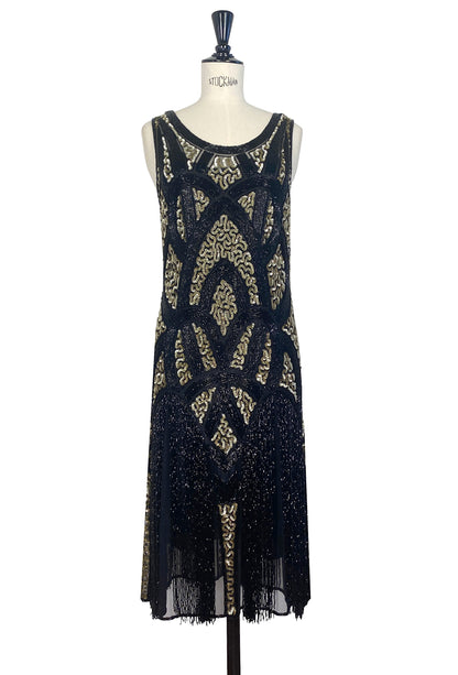 Black and gold sequin sleeveless dress with ornate pattern and fringe hem