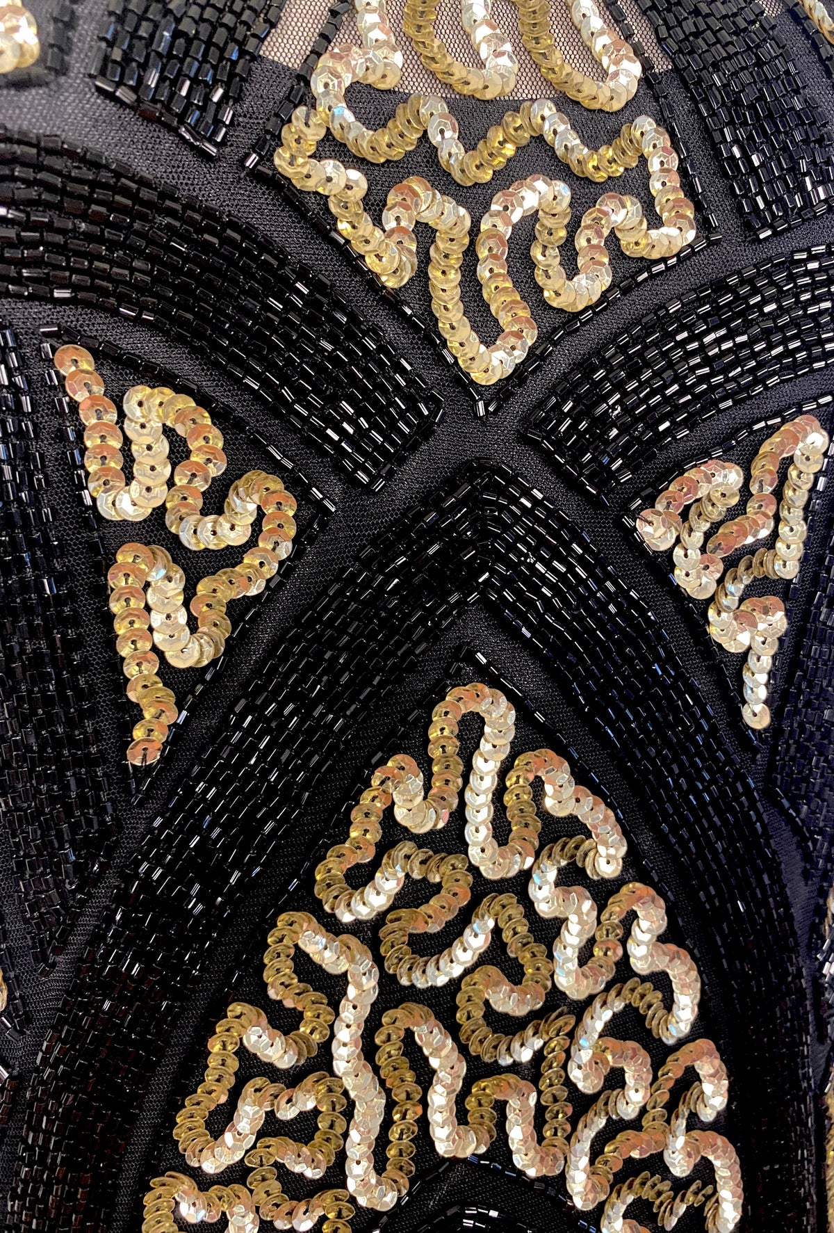 Close-up of black beaded bodice with gold sequins and ornate V-shaped trim