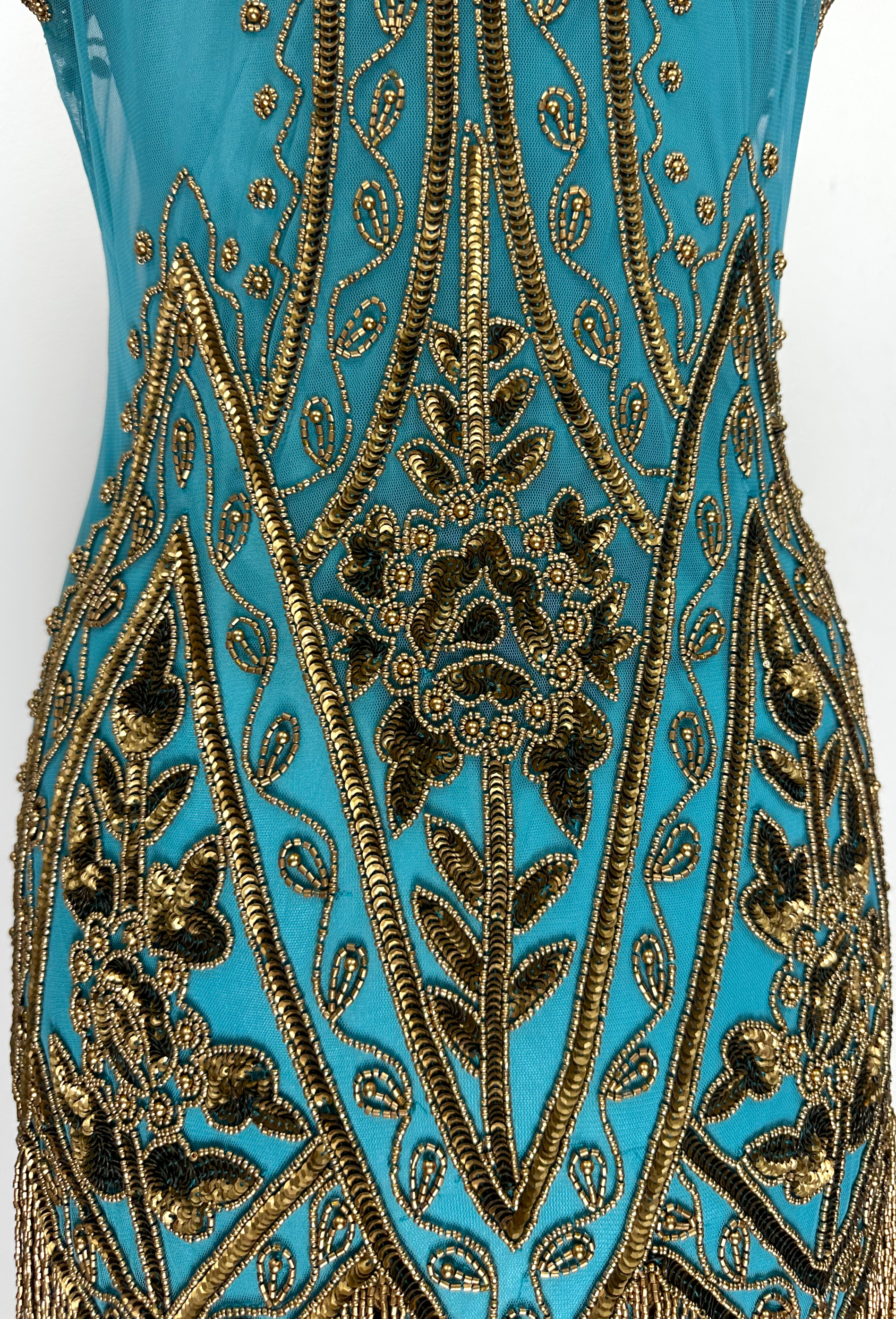 Close-up teal gown with ornate gold bead embroidery and scalloped trim