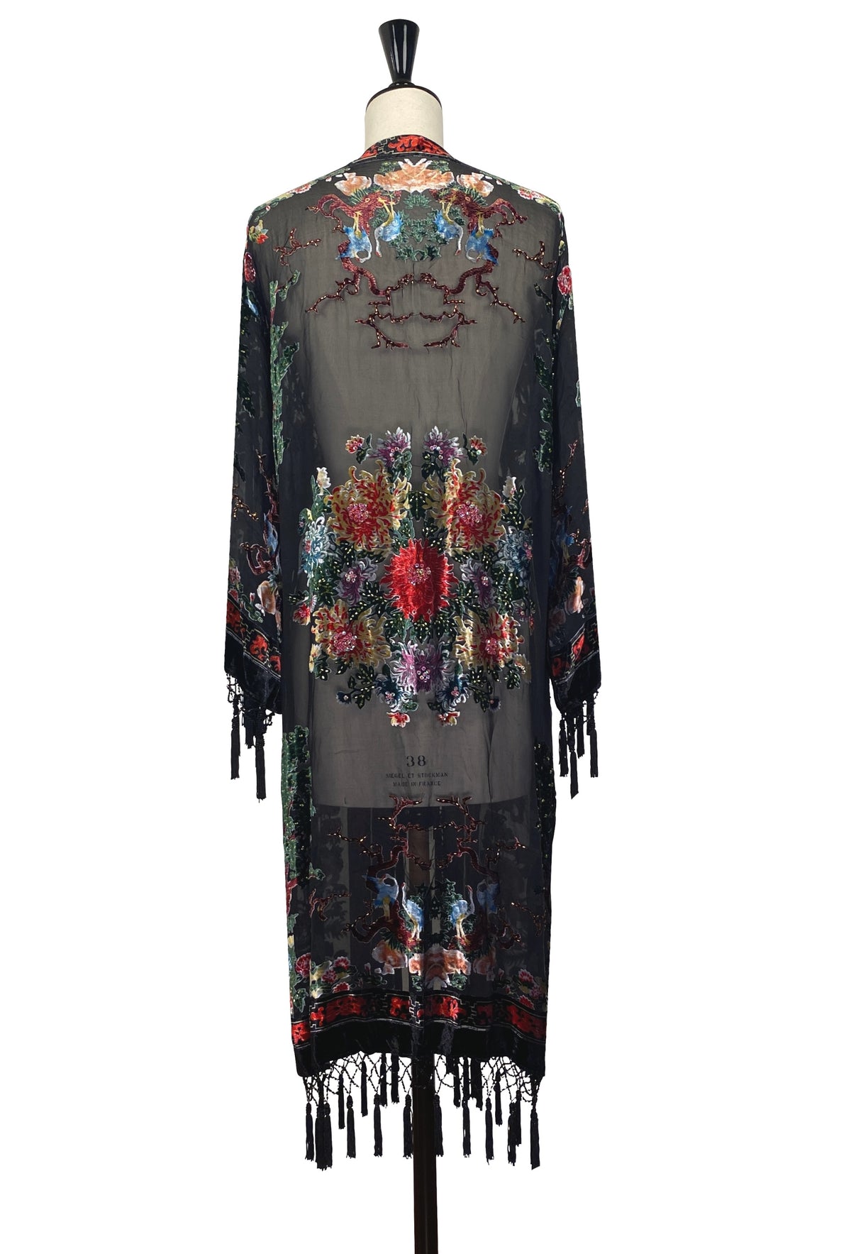 Embroidered floral kimono with tassel fringe, back view on dark fabric with colorful garden print